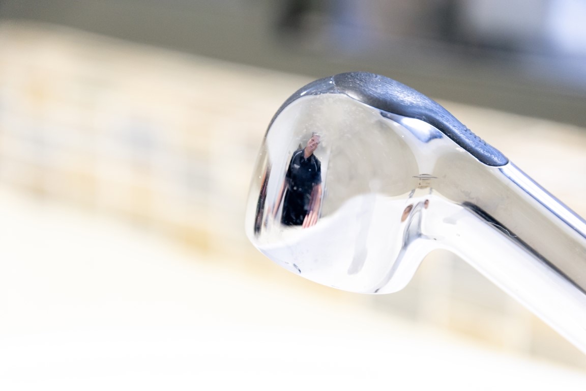 Close-up of a polished chrome tap spout with a plumber reflected in it