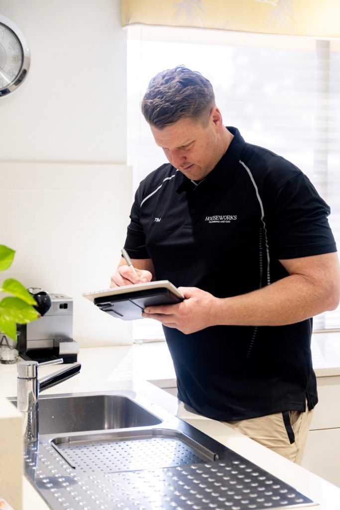 Plumber writing up a quote on a notepad beside a double stainless kitchen sink